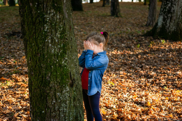在秋天的公园里，小女孩站在树旁玩捉迷藏图片下载