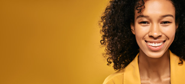 年轻的卷发女人的肖像，在热黄的背景与空白的空间带着牙齿的微笑。快乐的非裔美国妇女图片下载