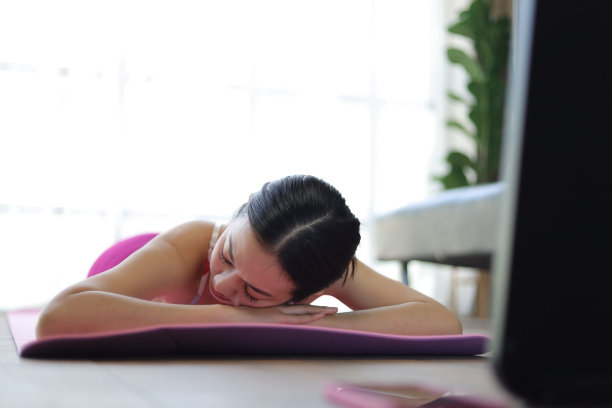 美丽的亚洲女人躺在铺着地毯的地板上，在家里的客厅里做瑜伽。图片下载
