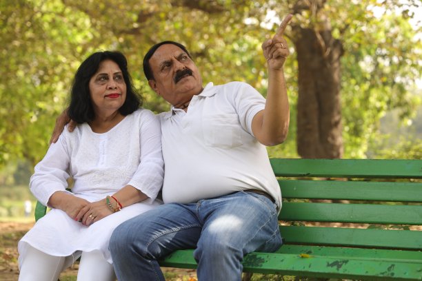 一对幸福的印度夫妇坐在公园的长椅上，丈夫指着什么。图片下载