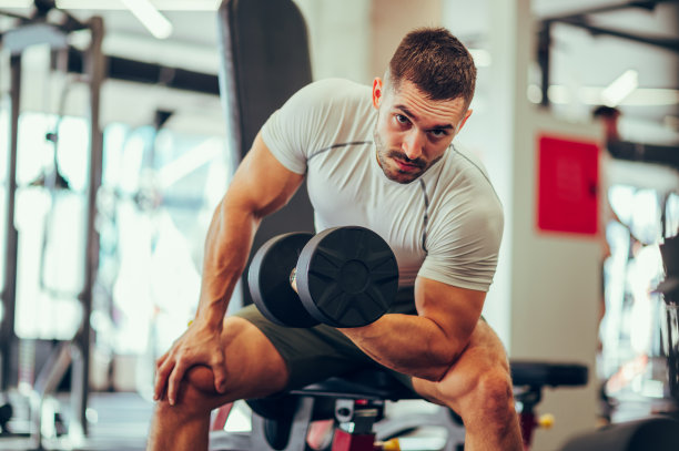 一个很有魅力的年轻运动员坐在体育中心，一边看着镜头一边锻炼肌肉。图片下载