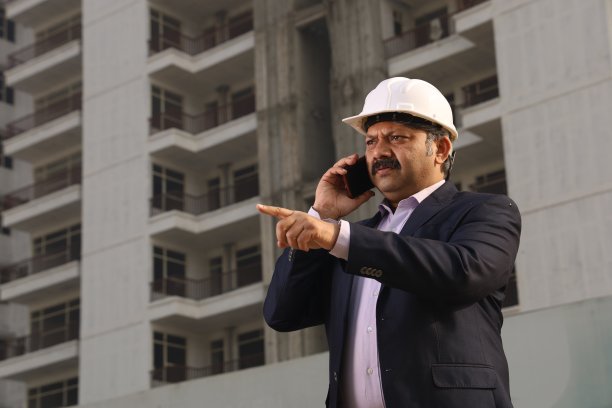 一个快乐的印度建筑工人戴着建筑工人的头盔站在一个建筑商的财产前。工程师安全帽。图片下载