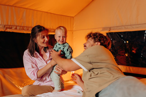 快乐的家庭和可爱的宝宝一起玩耍，在夏天的晚上躺在床上享受舒适的豪华野营。豪华露营帐篷，适合户外休闲娱乐图片下载