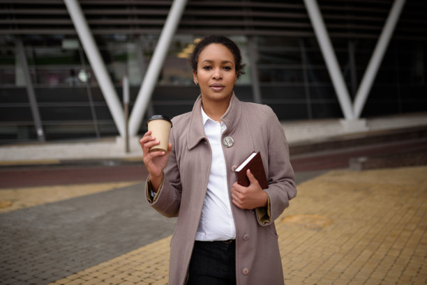 快乐的非裔美国妇女穿着职业装，带着笔记本和咖啡去办公室开会图片下载