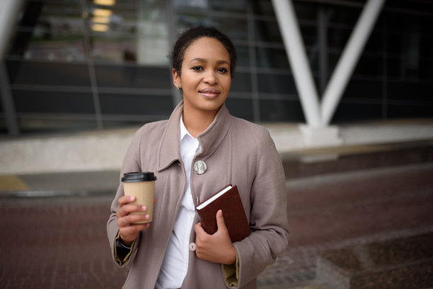 快乐的非裔美国妇女穿着职业装，带着笔记本和咖啡去办公室开会图片下载