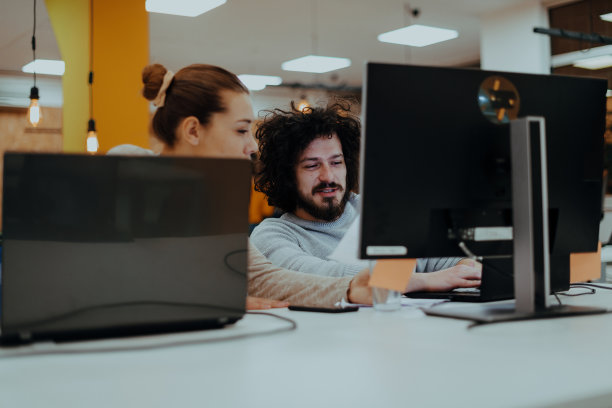 两个同事在现代创业公司的办公室里做一个项目。一个留着非洲式发型的男人和一个在办公室工作的金发女员工。图片下载