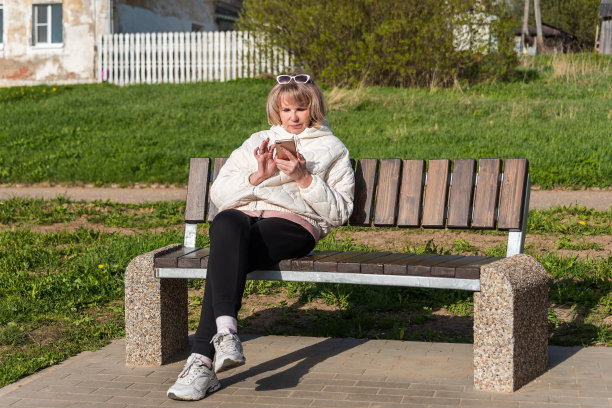 在公园或庭院的长椅上，有智能手机的成熟迷人的成年女性。图片下载