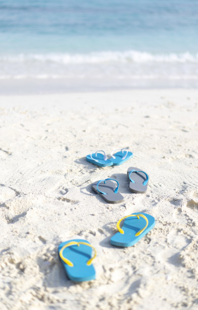 三双人字拖在马尔代夫的海滩上，背景是海洋。家庭度假图片下载