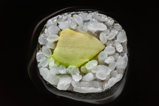 海苔包牛油果卷。卷放在一个白色的圆形陶瓷板上。盘子放在有图案的木桌上。旁边是一个盛着酱油的陶瓷碗。在碗里加入酱油。有一卷牛油果。图片下载