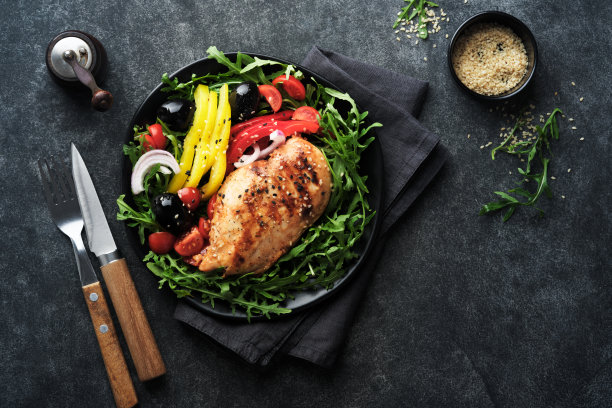 沙拉与烤鸡柳与新鲜芝麻菜，西红柿和橄榄在黑色盘子在旧的深色背景。鸡肉配沙拉。生酮午餐。健康食品。前视图。图片下载