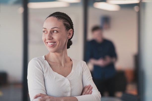 年轻微笑的商业女性在创意开放空间联合创业办公室的肖像。成功的女商人站在办公室拿着广告版面。在后台工作的同事。图片下载