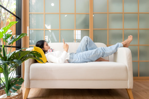 居家生活方式的女人躺在客厅的沙发上放松。快乐的女孩玩笔记本电脑，舒适的枕头，在周末假期小睡，健康和健康。生活方式的概念图片下载