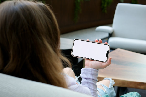 穿着蓝色毛衣的年轻女子站在窗户附近，使用带有预键白色屏幕的手机。很少有上下滚动、轻拍、放大和缩小的手势。图片下载