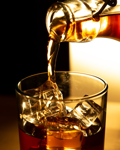 戏剧性的垂直视图，一个瓶子的剪影倒威士忌的玻璃杯与冰块图片下载