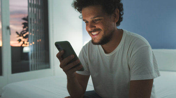 男人坐在卧室的床上，用手机看视频、电影图片下载