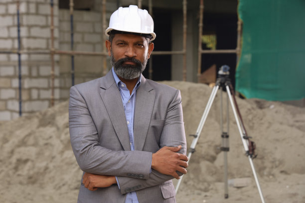 努力工作的印度工地工程师正在计算工作进度。在现场位置穿着制服和白色头盔。时尚张扬的工程师在施工现场，努力工作。图片下载