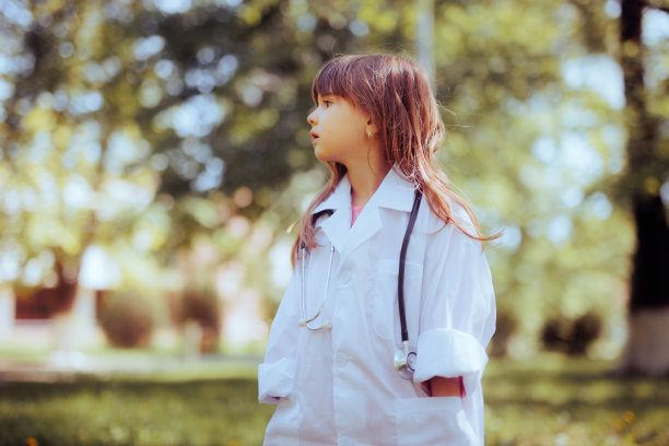 蹒跚学步的女孩穿着白色的医生服，戴着听诊器图片下载