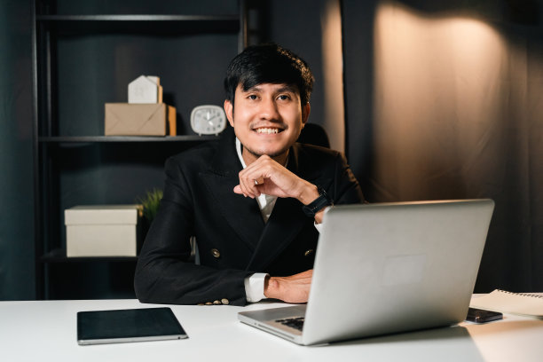 年轻的亚洲商人晚上在黑暗的办公室里用笔记本电脑工作。迷人英俊的印度男人在深夜带着落地灯的温暖灯光在家里努力加班图片下载