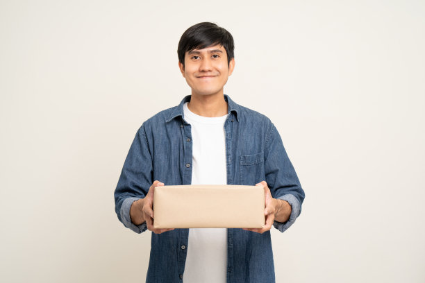 年轻兴奋的亚洲人拿着许多包裹纸板站在孤立的白色背景上。兴高采烈的男性拿着一大堆快递员送来的包裹箱图片下载