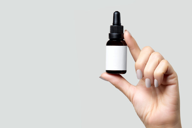 美容护肤理念。女人的手拿着一个玻璃化妆品瓶，上面空着你设计的标签。孤立的灰色背景与复制空间图片下载