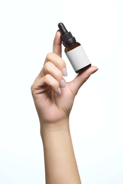 美容护肤理念。女人手拿着玻璃化妆品瓶的模型，空标签供你设计。在白色背景上与复制空间隔离。垂直格式图片下载