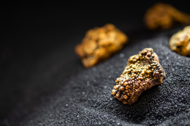 从矿井里挖出来的纯金被放在黑色的沙子上。图片下载