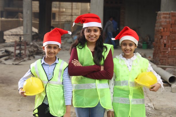 圣诞节那天，年轻的印度学校的孩子们在建筑商的建筑工地上作为模范工程师工作，他们正在绘制房屋的蓝图。他们戴着建筑工程师的头盔。戴着圣诞老人的帽子。圣诞快乐。图片下载