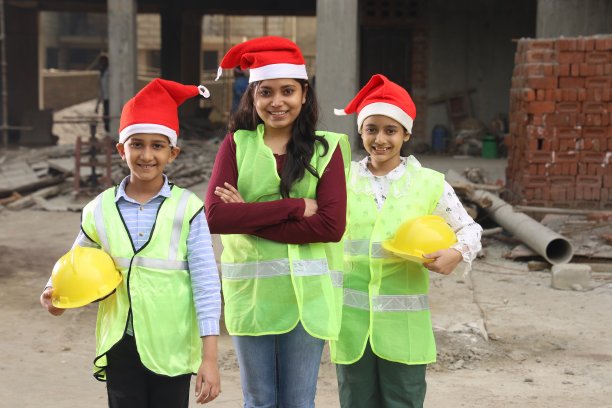 圣诞节那天，年轻的印度学校的孩子们在建筑商的建筑工地上作为模范工程师工作，他们正在绘制房屋的蓝图。他们戴着建筑工程师的头盔。戴着圣诞老人的帽子。圣诞快乐。图片下载