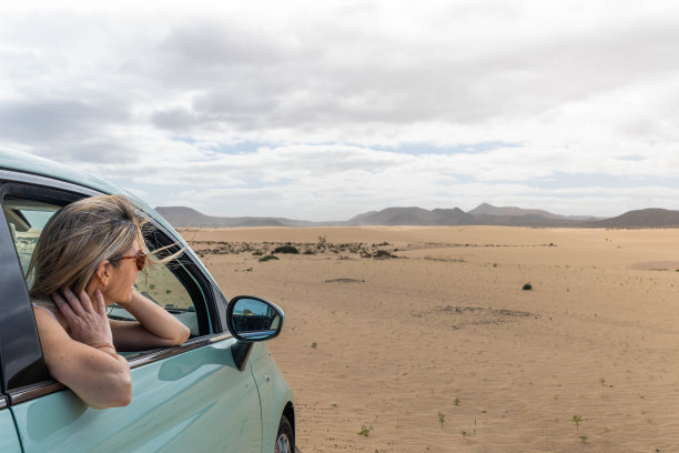一个金发女人坐在车里，从车窗往外看沙漠路上的风景图片下载