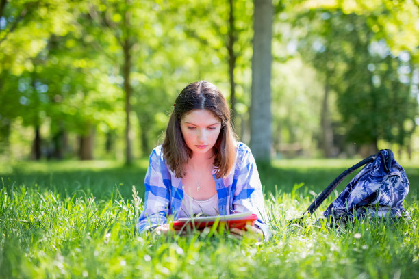 一个女学生坐在公园的草地上，在户外学习阅读笔记图片下载