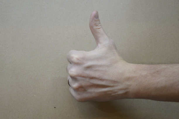 在棕色背景上，男性拇指向上的手特写图片下载