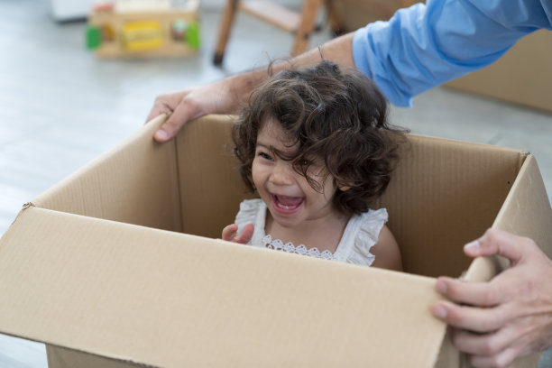 搬家、按揭、家庭、房地产概念。快乐的父亲和可爱的小女儿，蹒跚学步的女婴在纸箱里玩耍，一家人搬进了新居图片下载