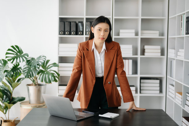 年轻迷人的亚洲女性白领，正西装革履，在现代办公室对着镜头微笑图片下载