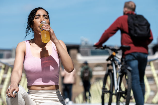 运动女人坐在地板上用瓶子喝酒。图片下载