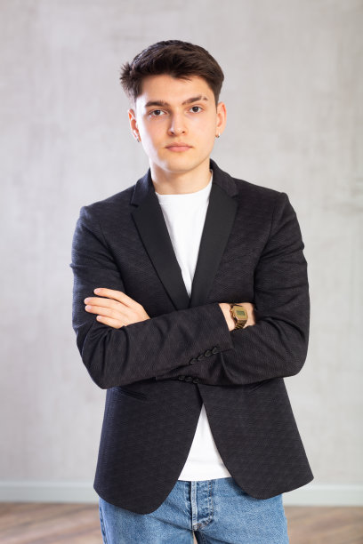 穿着黑色夹克的积极的男学生摆姿势，双臂交叉在胸前，灰色背景图片下载