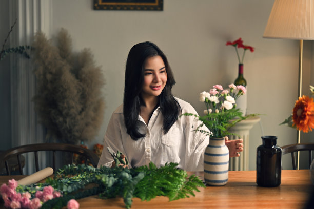 迷人的亚洲女子正在插花花瓶装饰她的客厅图片下载