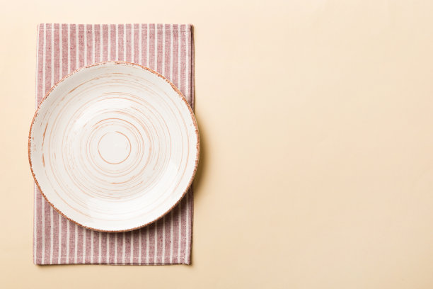 彩色背景上的俯视图，桌布上的空圆形白色盘子盛食物。空盘子放在餐巾上，为你的设计留出空间图片下载