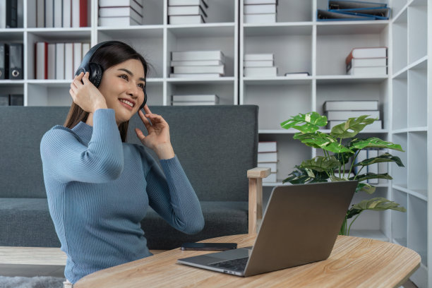 放松的女人在家里用笔记本电脑戴着耳机听音乐图片下载