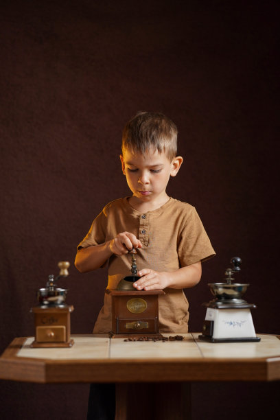 一个孩子在一个复古的咖啡研磨机上准备咖啡。一个小帮手。工作室照片在棕色色调与侧光。图片下载