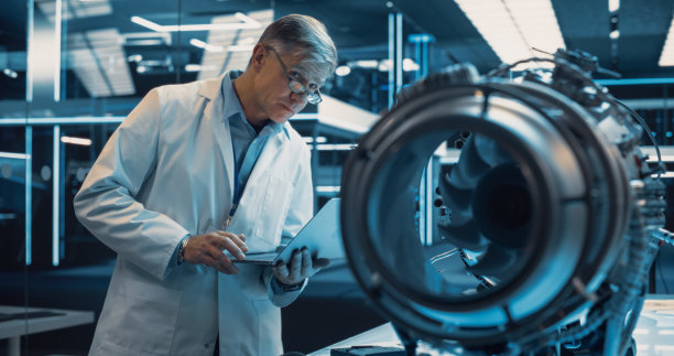 一位戴眼镜的中年工业涡轮机专家，带着一项创新发明站在桌子旁。博士教授利用笔记本电脑开发高科技原型电机图片下载