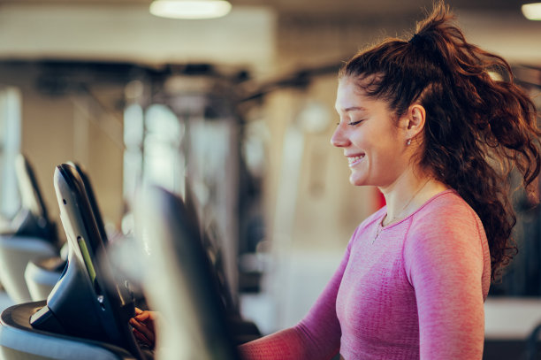 一个快乐的女运动员在健身房开始跑步机。图片下载