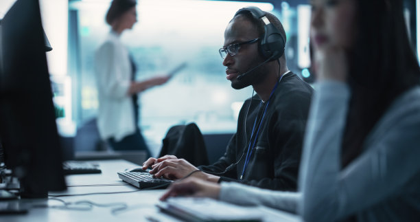 一个聪明的非洲年轻专家在技术创业服务台部门工作的肖像，在一个多样化的办公室使用计算机。戴着眼镜和耳机还有麦克风的黑人男子图片下载