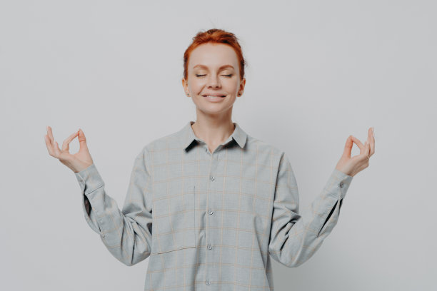 平静的红发女人，穿着格子衬衫，双手做着手印的姿势，闭着眼睛在冥想图片下载