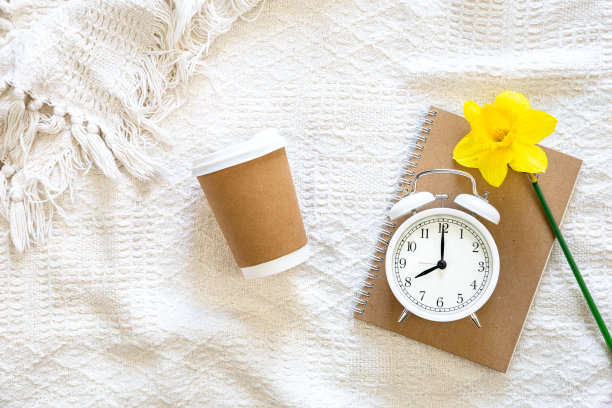 床上的纸杯、笔记本和白色闹钟，俯视图。图片下载