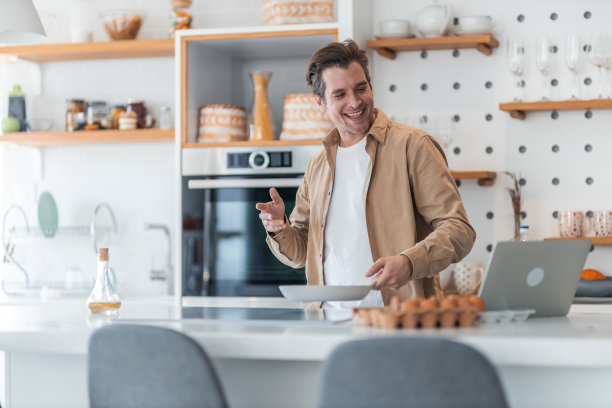 一位面带微笑的商人正在与同事进行在线视频通话，并在做早餐。图片下载