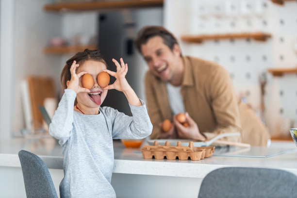 一个有趣的小女孩在爸爸做早餐的时候玩鸡蛋的照片。图片下载