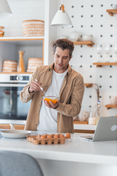 一名男性自由职业者在碗里打鸡蛋，做煎蛋卷作为早餐。图片下载
