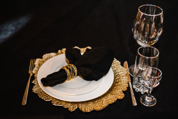 上菜，摆餐具。盘子装饰亚麻黑色餐巾和银器餐具，玻璃杯。侧视图。特写镜头。婚礼布置，餐桌接待。生日，洗礼，大事。奢华的金色装饰。图片下载