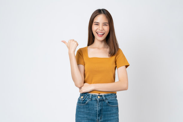 快乐微笑的年轻女子穿着休闲的橙色t恤，一只手指着一边，孤立在白色的背景上。图片下载
