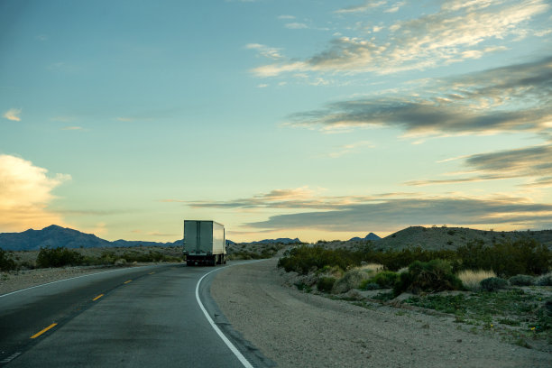 一辆半挂车行驶在两车道的公路上，夕阳下有美丽的云彩图片下载